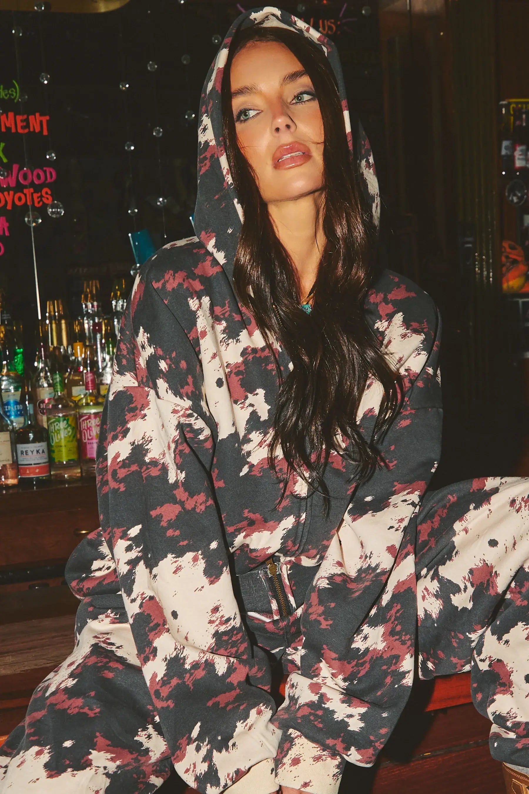 Person wearing a COW patterned hoodie in a bar setting